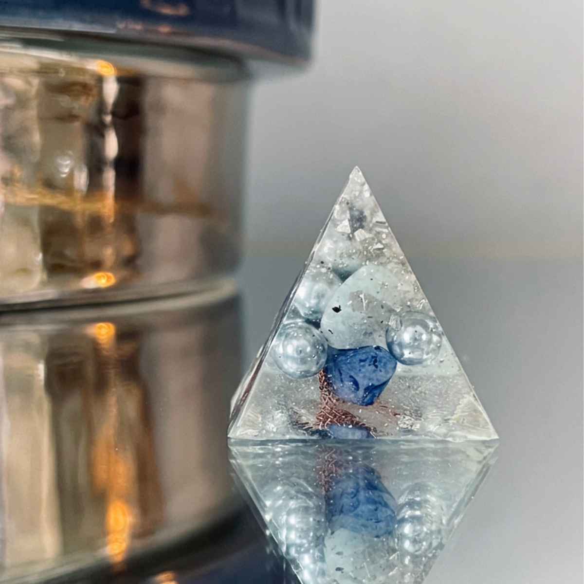 a white, blue, and copper organite crystal on a reflective surface with gold shimmer in the background