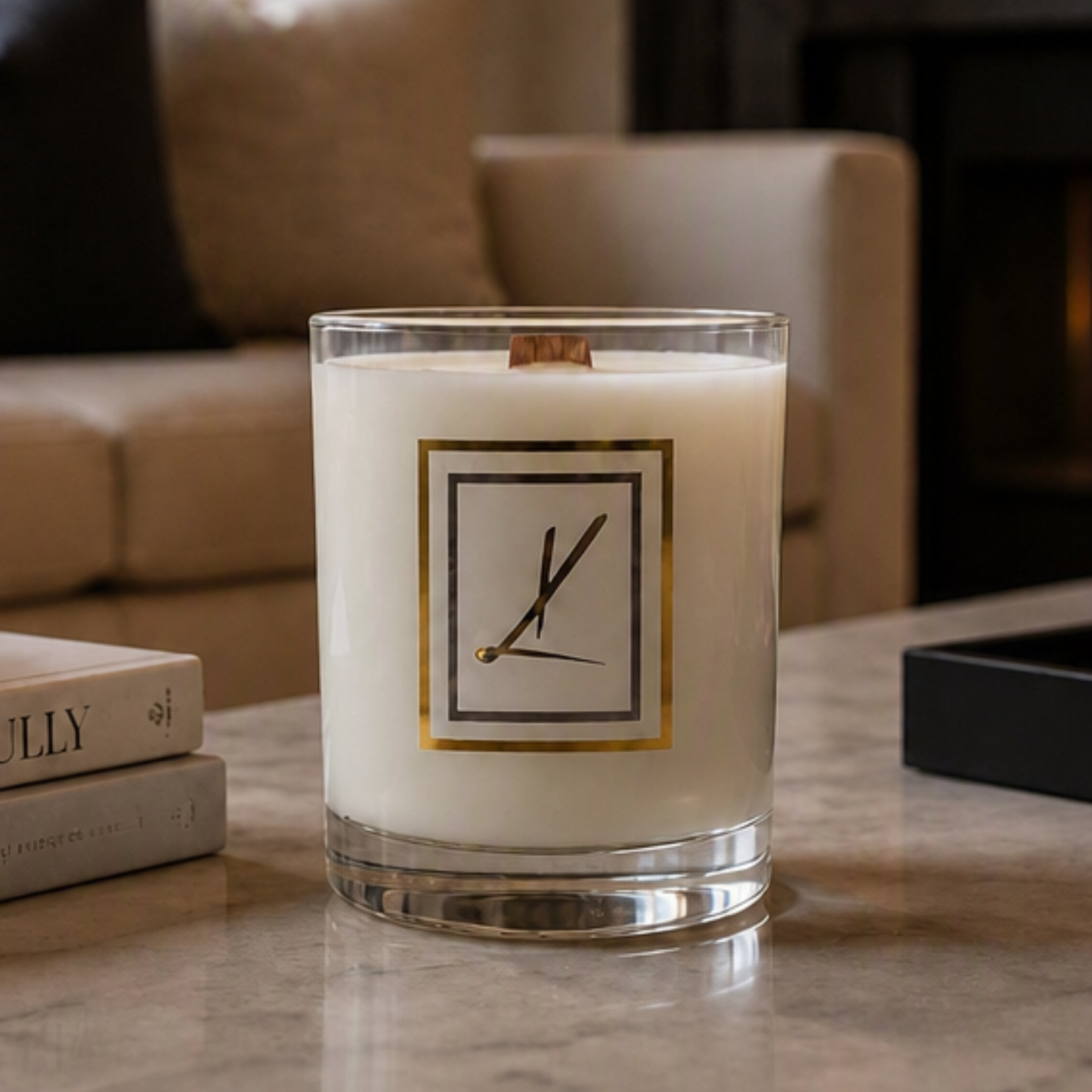 A white candle in a clear glass jar with a Karys Layne logo on the front, set on a marble tabletop next to stacked books in a cozy living room setting. Choose your scent