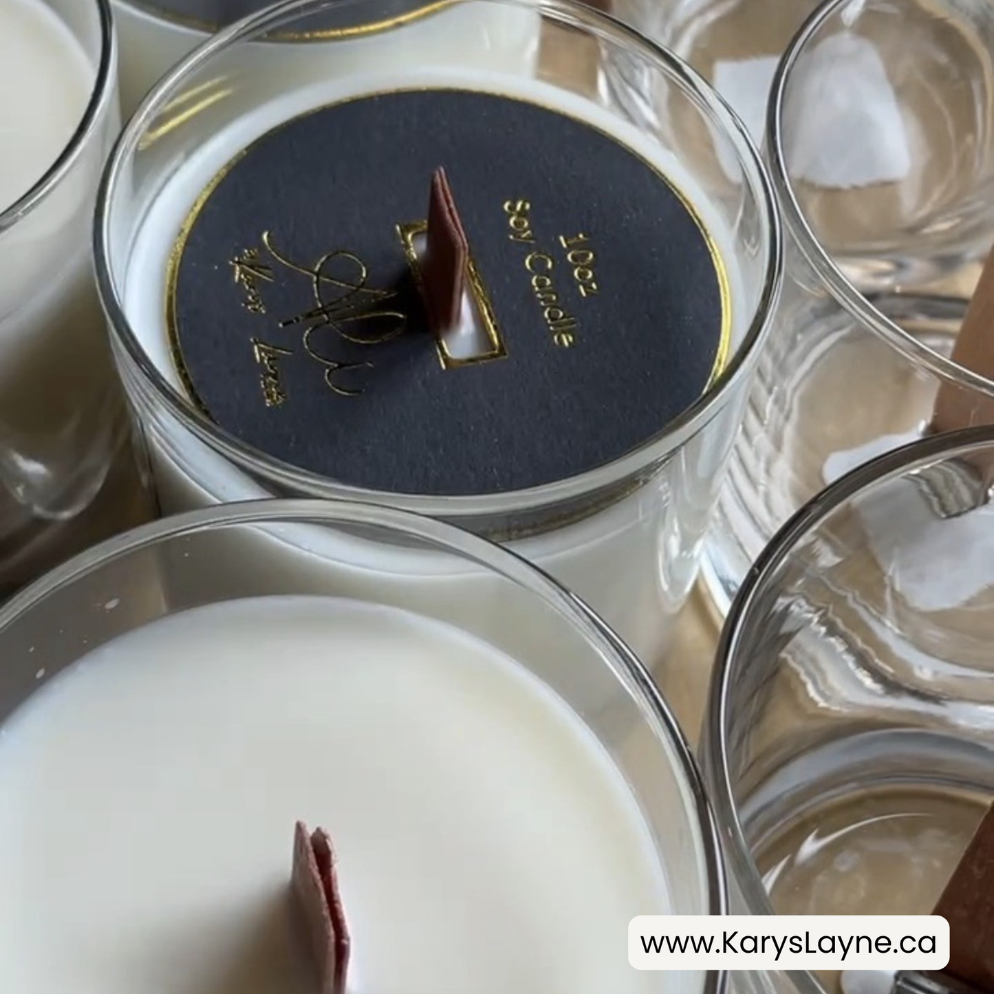 A close-up of several Karys Layne Candles glass jars with white wax and dark labels. One label is visible and reads '10oz Candle' with gold lettering, and wooden wicks and soy wax.