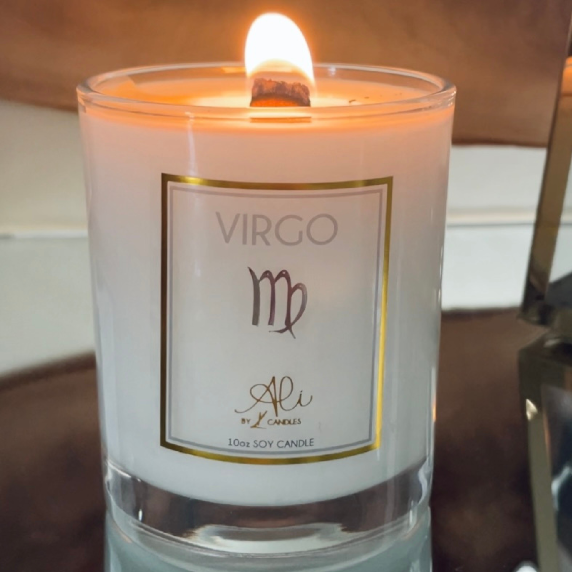 A lit white soy candle in a clear glass jar with a gold-bordered label reading VIRGO and Ali by Karys Layne Candles shown close up with the flame visible.